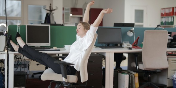 Vrouw met benen op bureau rekt zich uit want het is allemaal wel goed zo